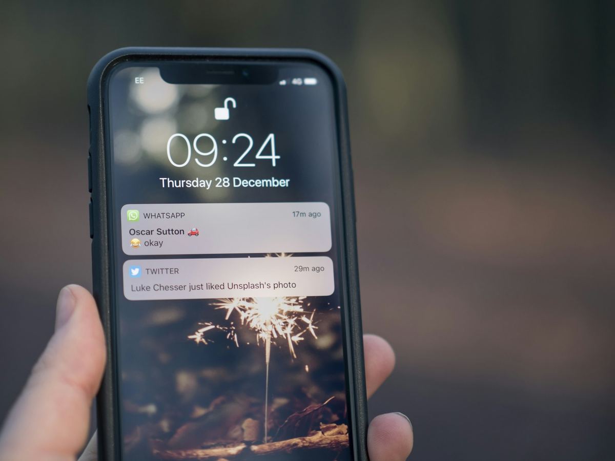 Tangan memegang ponsel dengan layar kunci yang menampilkan dua notifikasi pesan masuk